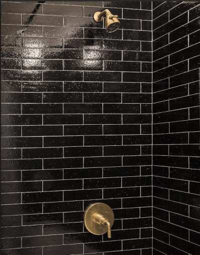 a black and gold tiled shower with a brass faucet.