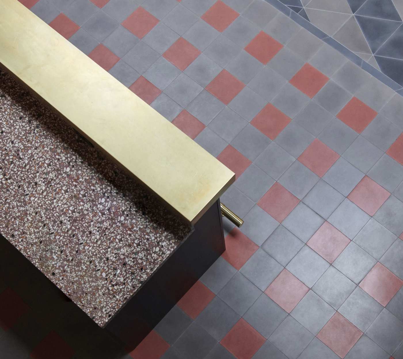 a counter with a gold top in a room with a red and grey tile floor.