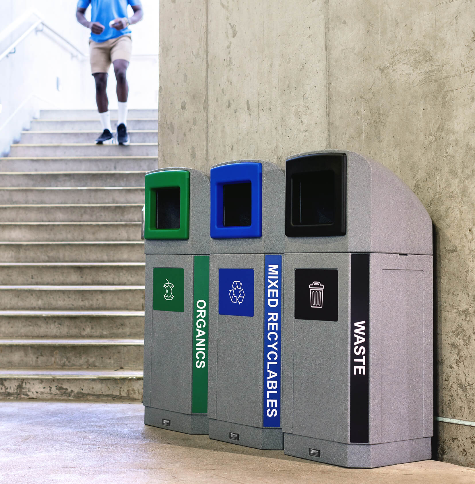 triple waste and recycling station with canopy lids and colored trim openings with matching labels at a transit station