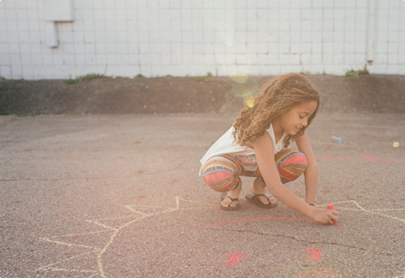 A child drawing a sun with a smiley face on the ground with chalk.