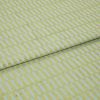 Textile fabric with raised yellowâ€‘green rectangular grid pattern, folded once along a horizontal seam and overlapping, close-up studio-lit sample on a pale blue ground, showing textured weave.
