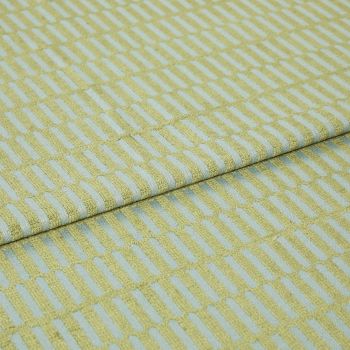 Textile fabric with raised yellowâ€‘green rectangular grid pattern, folded once along a horizontal seam and overlapping, close-up studio-lit sample on a pale blue ground, showing textured weave.