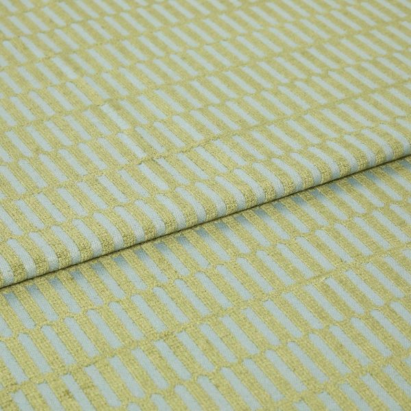 Textile fabric with raised yellow‑green rectangular grid pattern, folded once along a horizontal seam and overlapping, close-up studio-lit sample on a pale blue ground, showing textured weave.