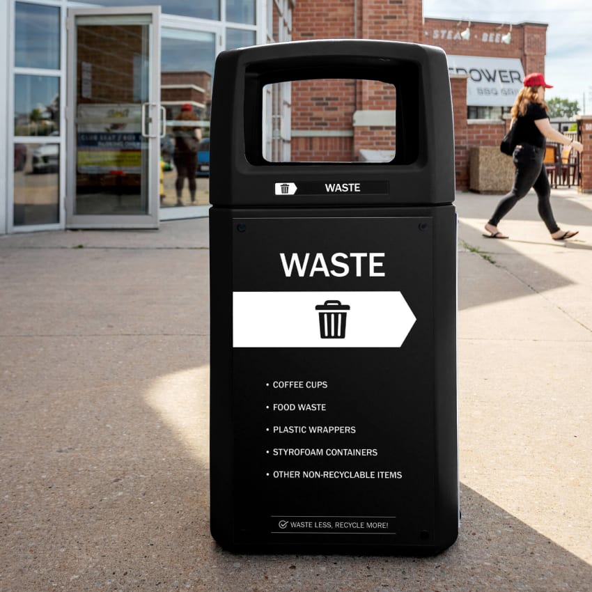 black waste bin made from post-consumer recycled plastic outside of a sports arena with body signs and labels