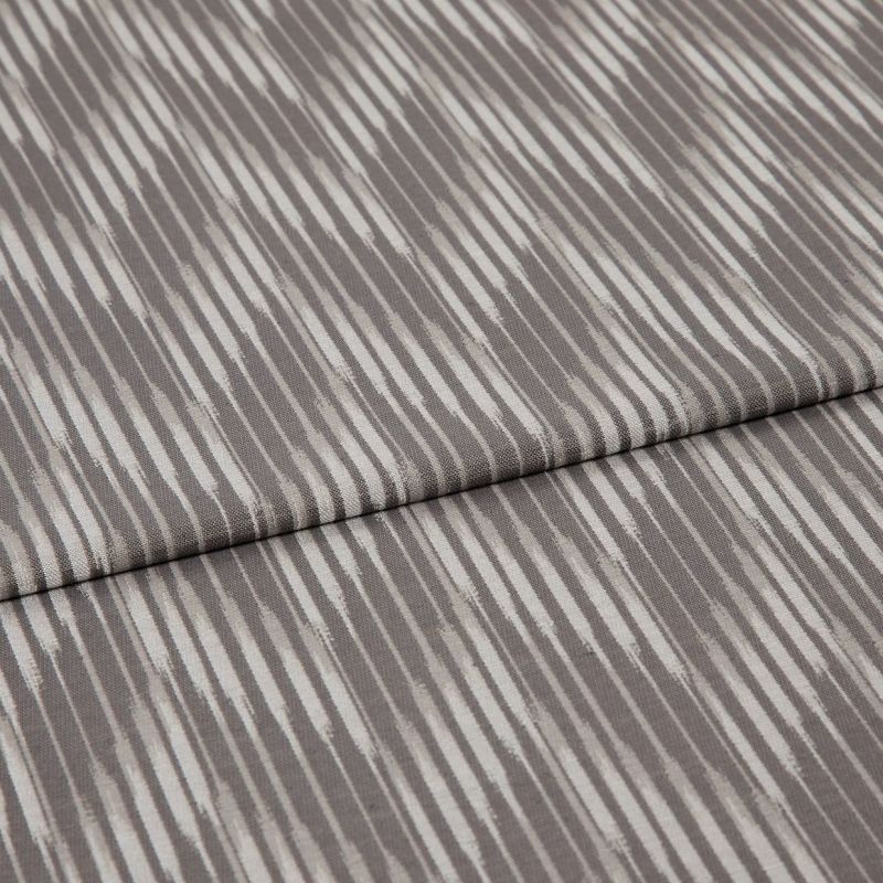 Folded curtain fabric sample with narrow, irregular vertical grey and off-white stripes; folded edge across center, shown close-up on a neutral surface under soft, diffuse lighting.