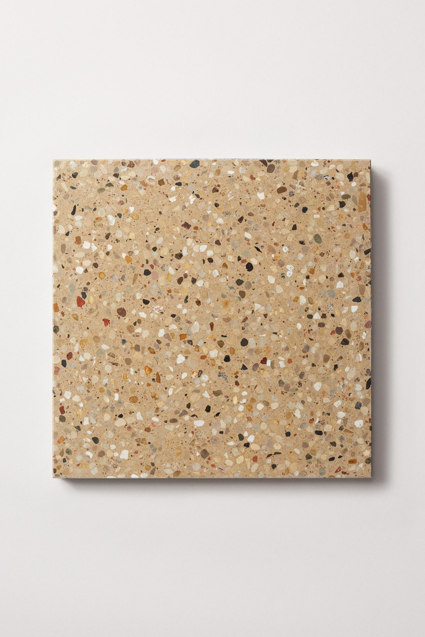 a square beige tile with a terrazzo pattern on a white surface.