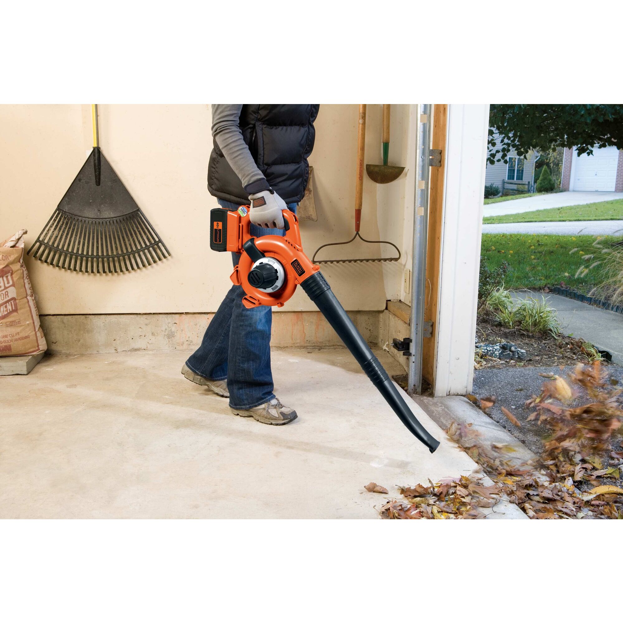 Man using Cordless Leaf Blower/Vacuum to blow leaves out of a garage.