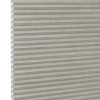 Honeycomb cellular fabric blind with horizontal pleats and textured beige finish, fully lowered and closed, diffusing soft light; set against a neutral, evenly lit wall with narrow white margin left.