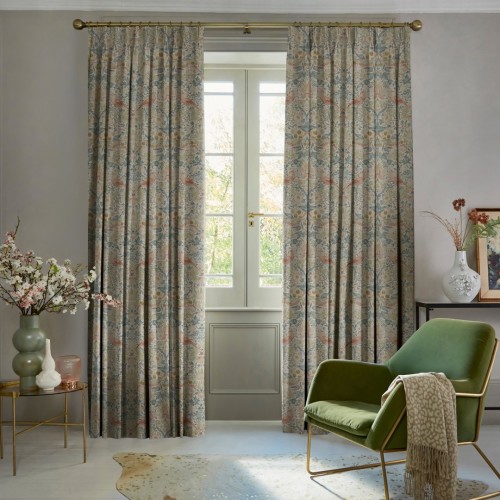 Patterned pleated full-length curtains on a brass rod, parted to reveal a French window, softly filtering daylight into a living room with green armchair, vases and a leafy garden view.