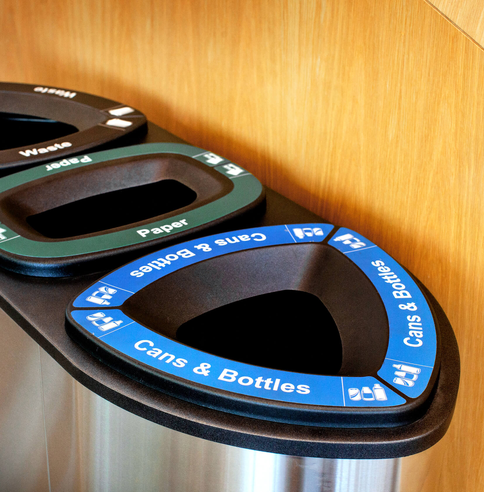 close up of cans and bottles recycling lid on a stainless steel container against a wood wall in a modern college campus