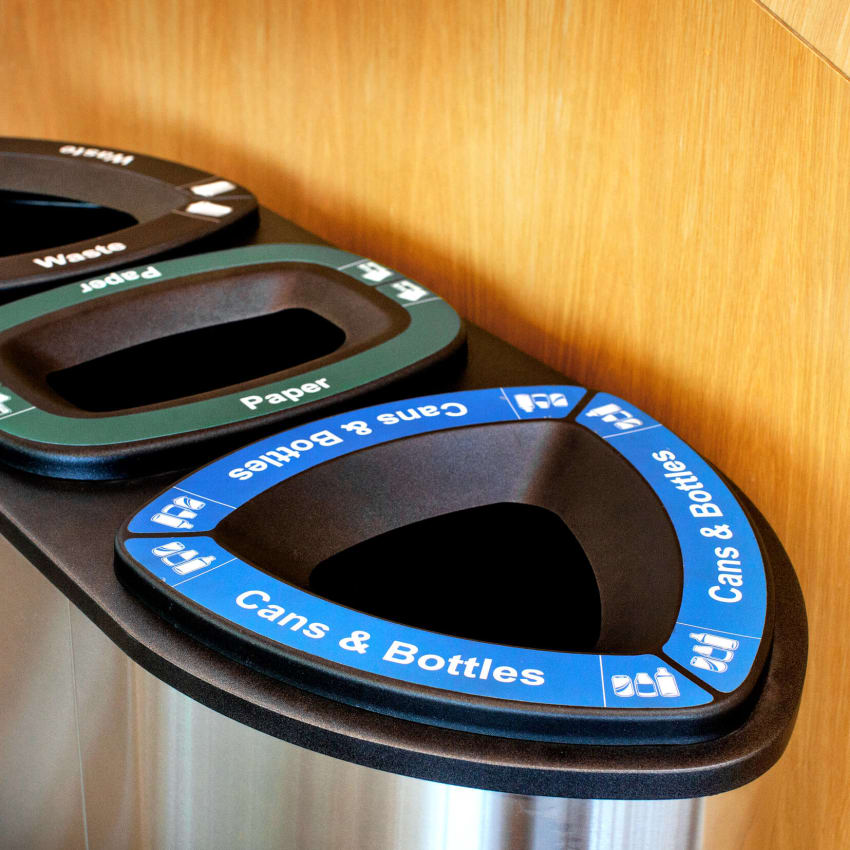 close up of cans and bottles recycling lid on a stainless steel container against a wood wall in a modern college campus