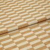 Woven beige-and-cream checkered fabric folded to create an overlapping edge, close-up studio-lit view highlighting the textured weave and repetitive rectangular pattern.