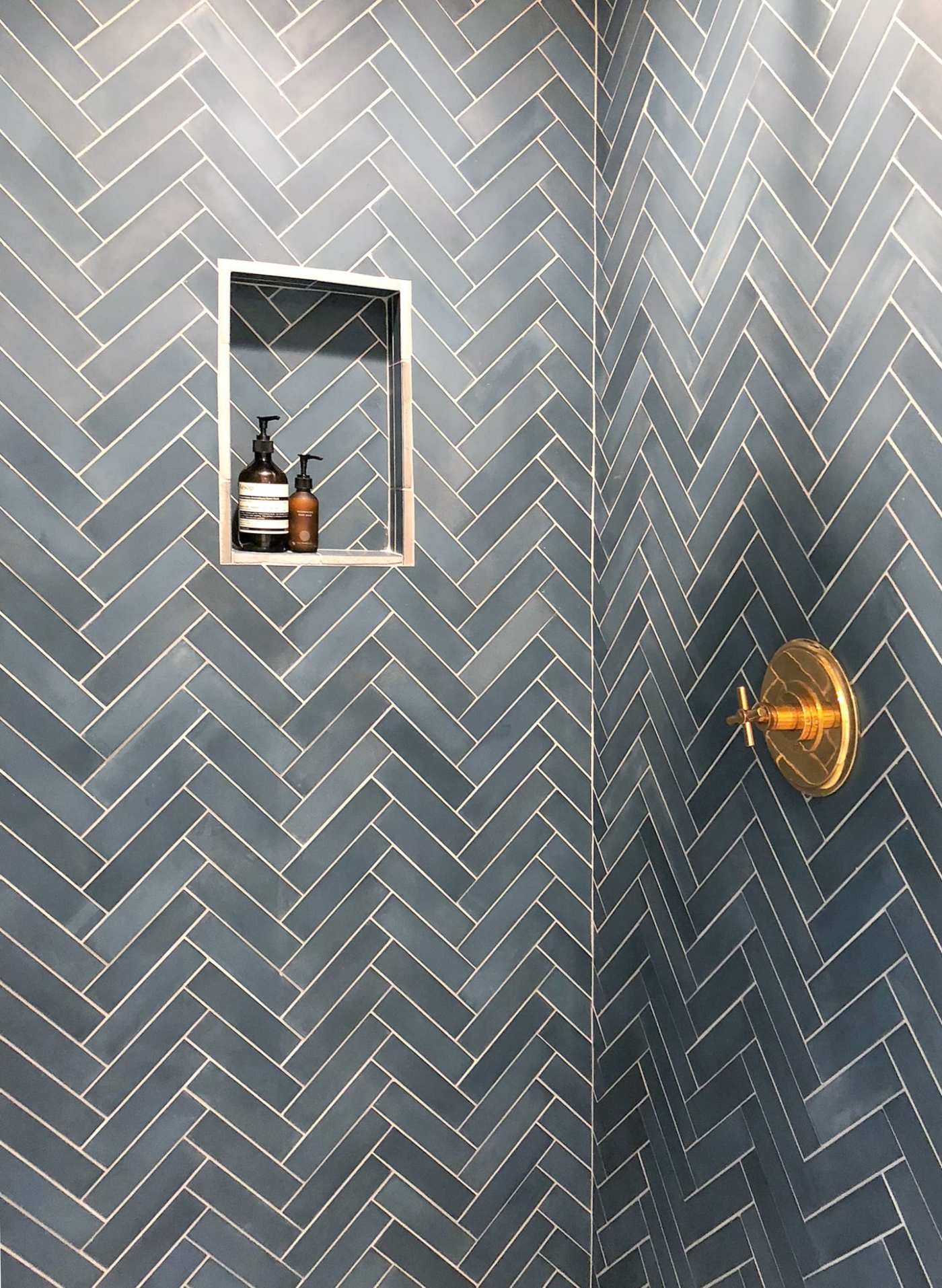 a blue herringbone tiled shower with a gold handle.