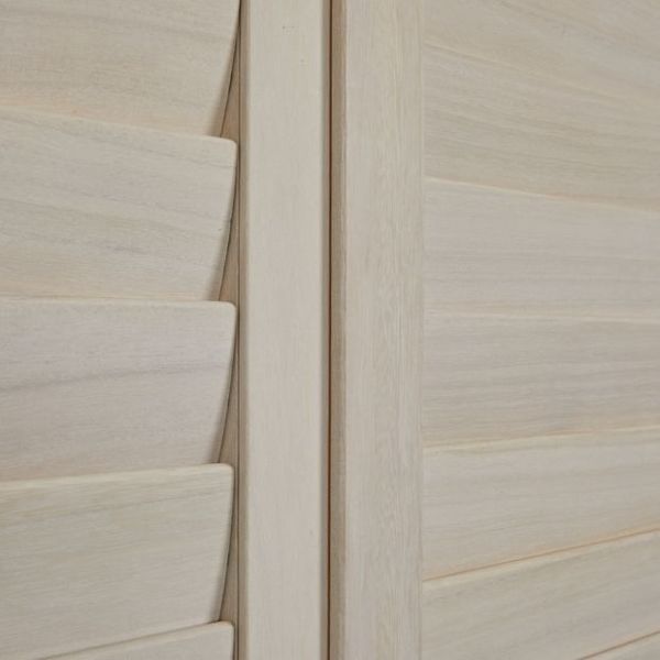 Pale wooden louvered shutters with a central vertical stile; left panel's slats are partially angled, right panel's slats closed, softly filtering interior light in a close-up of smooth wood grain.