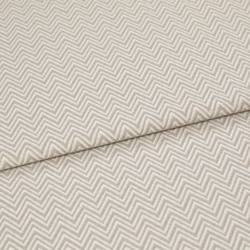 Beige chevron-embossed fabric folded diagonally, showing repeated raised zigzag pattern; close-up, evenly lit textile surface emphasizing texture and subtle two-tone threads.