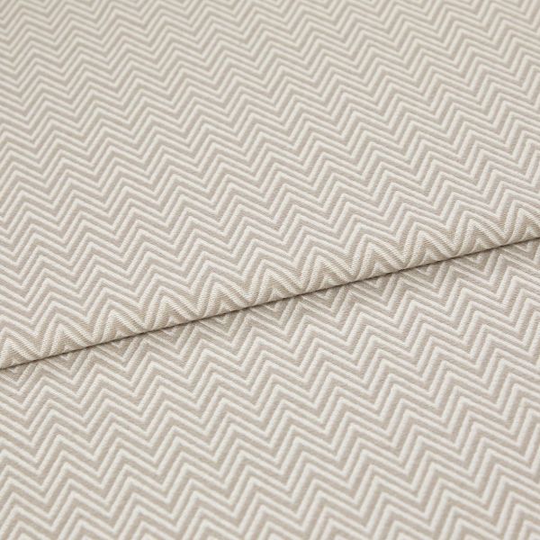 Beige chevron-embossed fabric folded diagonally, showing repeated raised zigzag pattern; close-up, evenly lit textile surface emphasizing texture and subtle two-tone threads.
