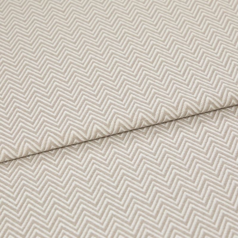 Beige chevron-embossed fabric folded diagonally, showing repeated raised zigzag pattern; close-up, evenly lit textile surface emphasizing texture and subtle two-tone threads.