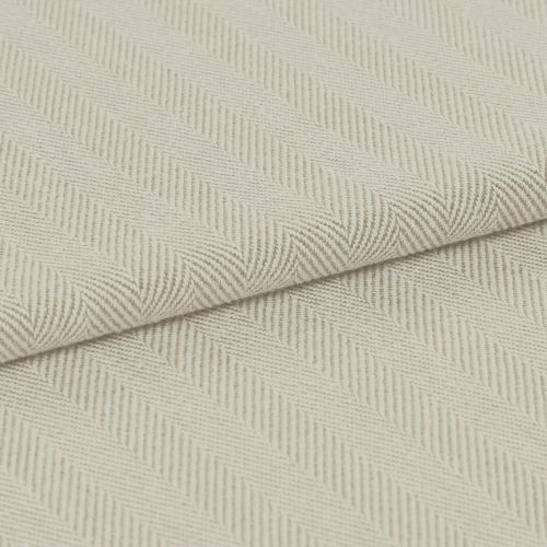 Cream herringbone-woven fabric folded diagonally, showing raised ribbed chevron pattern; laid flat under soft, even lighting for a close-up textile detail.