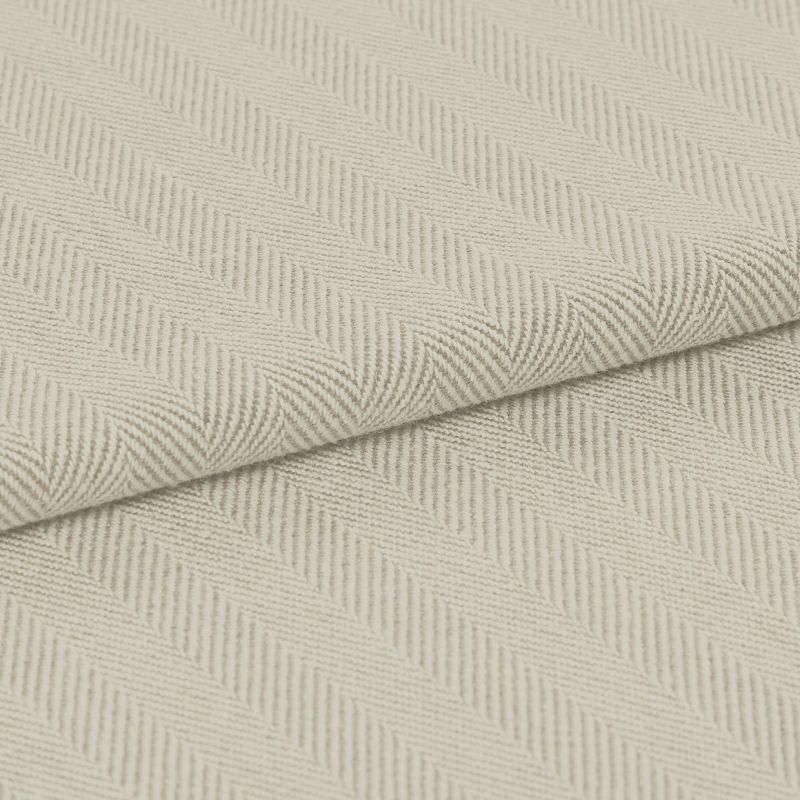 Cream herringbone-woven fabric folded diagonally, showing raised ribbed chevron pattern; laid flat under soft, even lighting for a close-up textile detail.