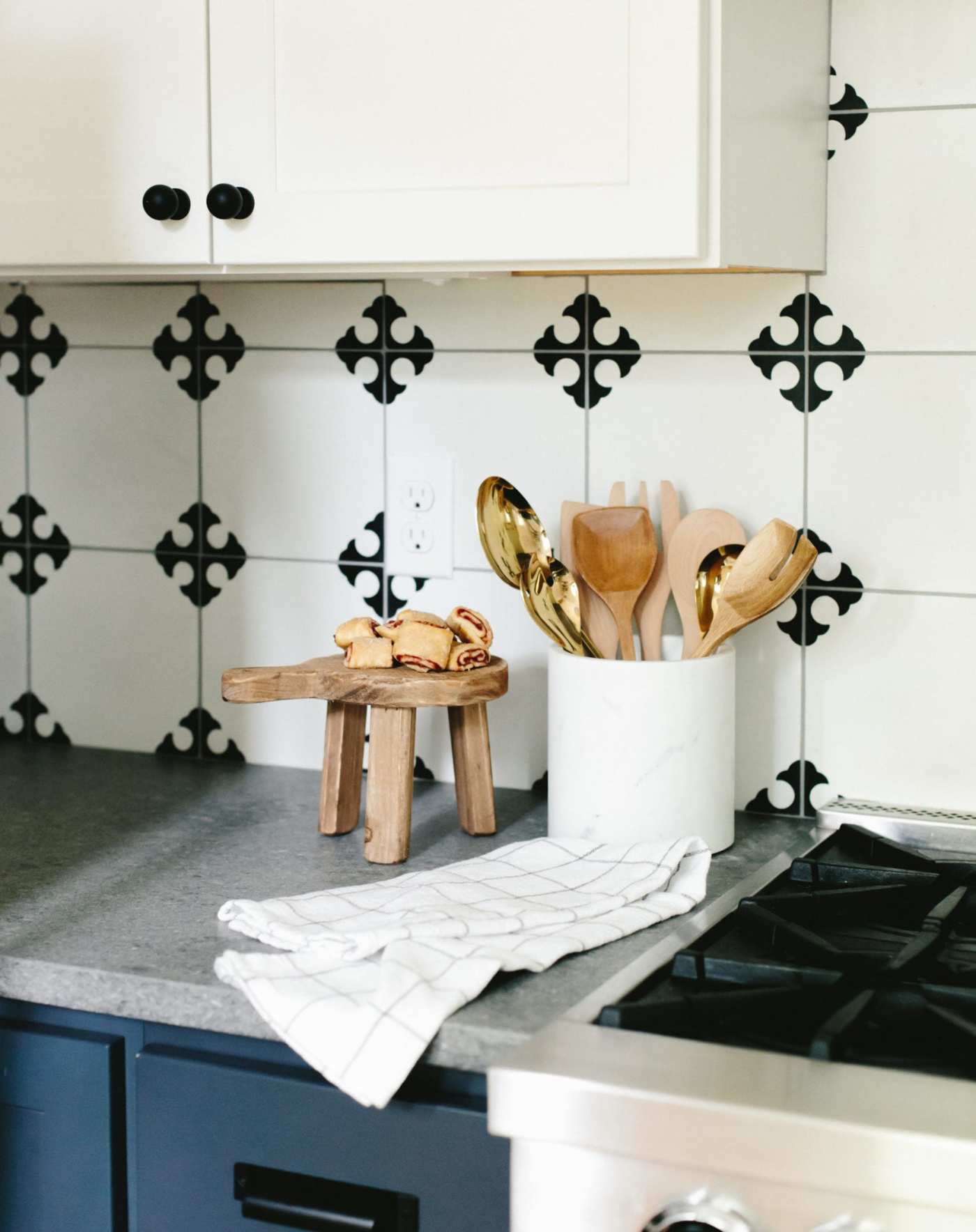 a kitchen counter with a black and white tiled backsplash and wooden utensils.