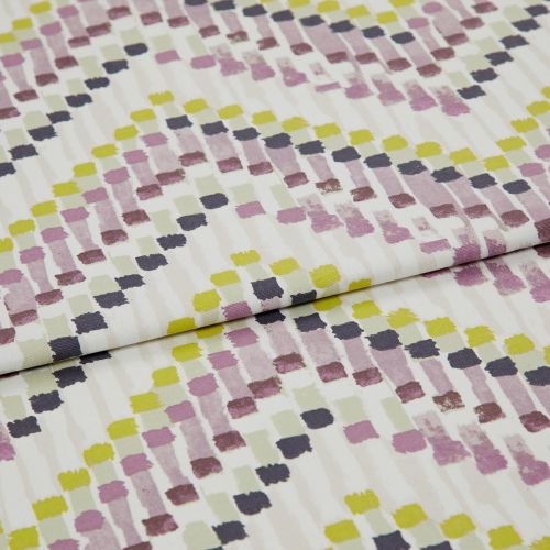 Folded cotton fabric with painterly square brushstrokes (mauve, chartreuse, olive, charcoal) arranged in staggered rows — folded across the frame, close-up on a flat surface under soft, diffuse lighting.