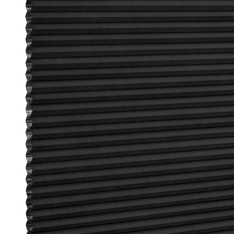 Black cellular (honeycomb) pleated blind, lowered and closed with left-edge cells exposed, blocking light; close-up studio product shot on neutral white background with even lighting.