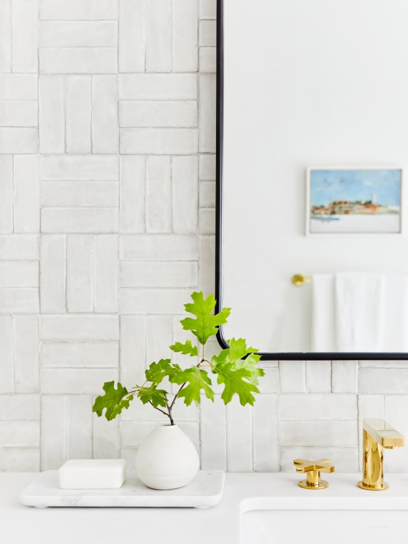 a white tiled bathroom with a plant and a mirror.