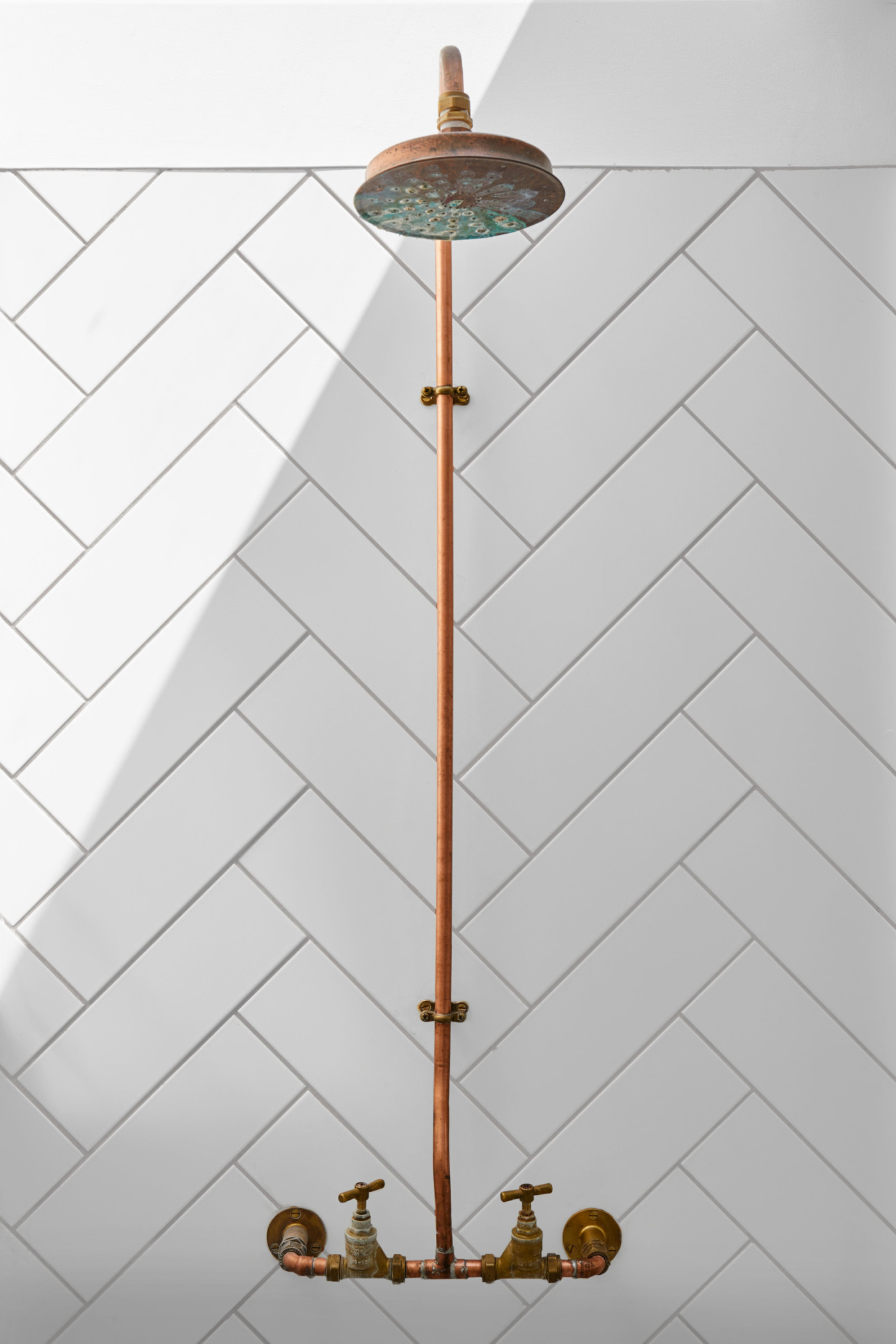 a white tiled bathroom with a copper shower head hanging on the wall.