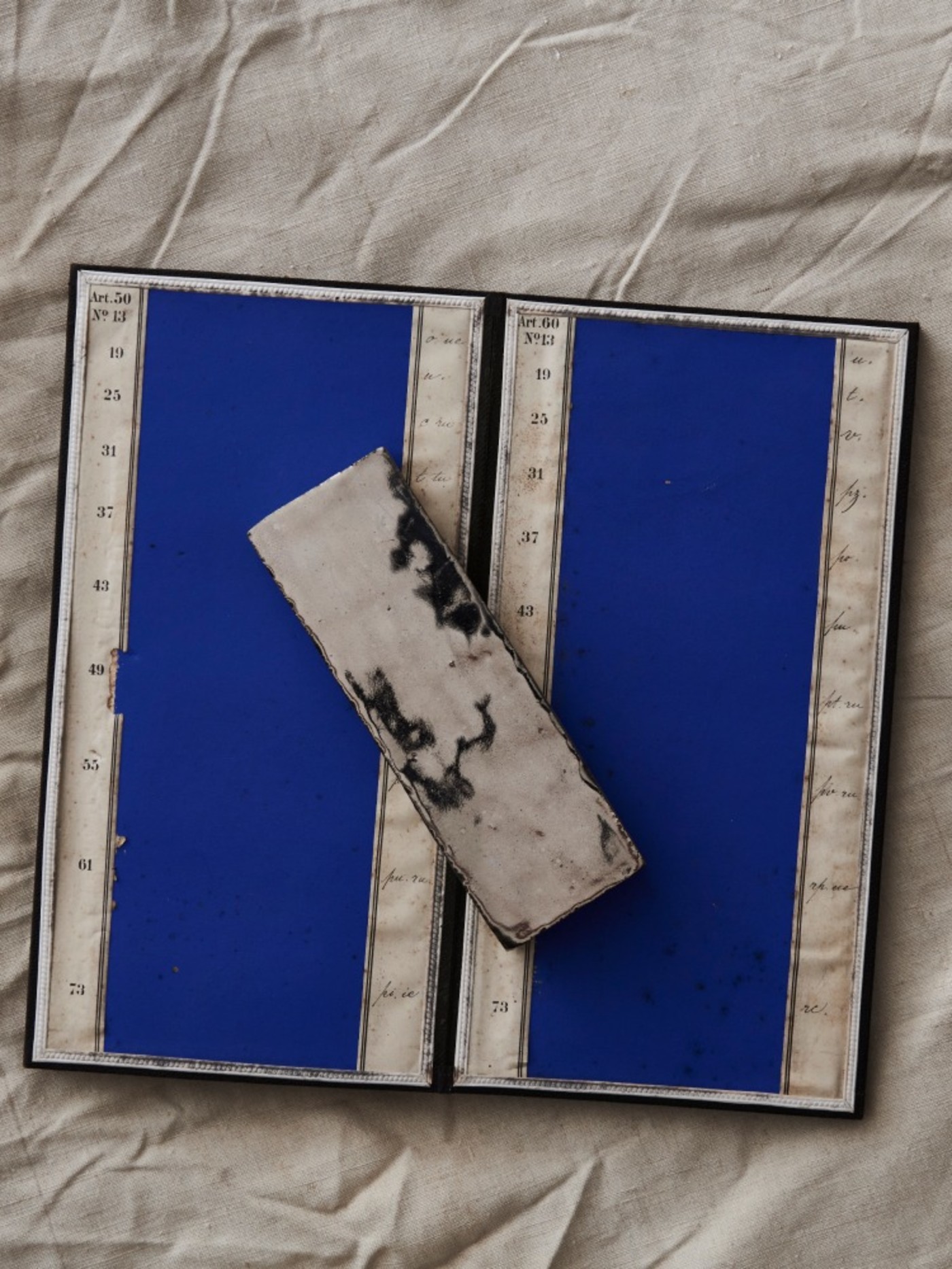 2 blue tiles and 1 white and black tile on a piece of beige cloth.