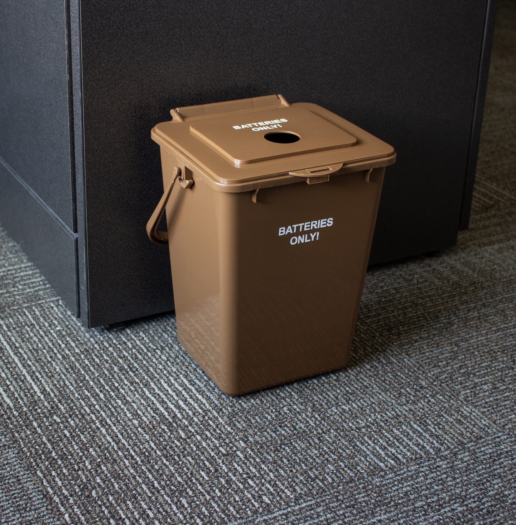 brown injection molded plastic bin for collecting used batteries placed on the floor in a corporate office