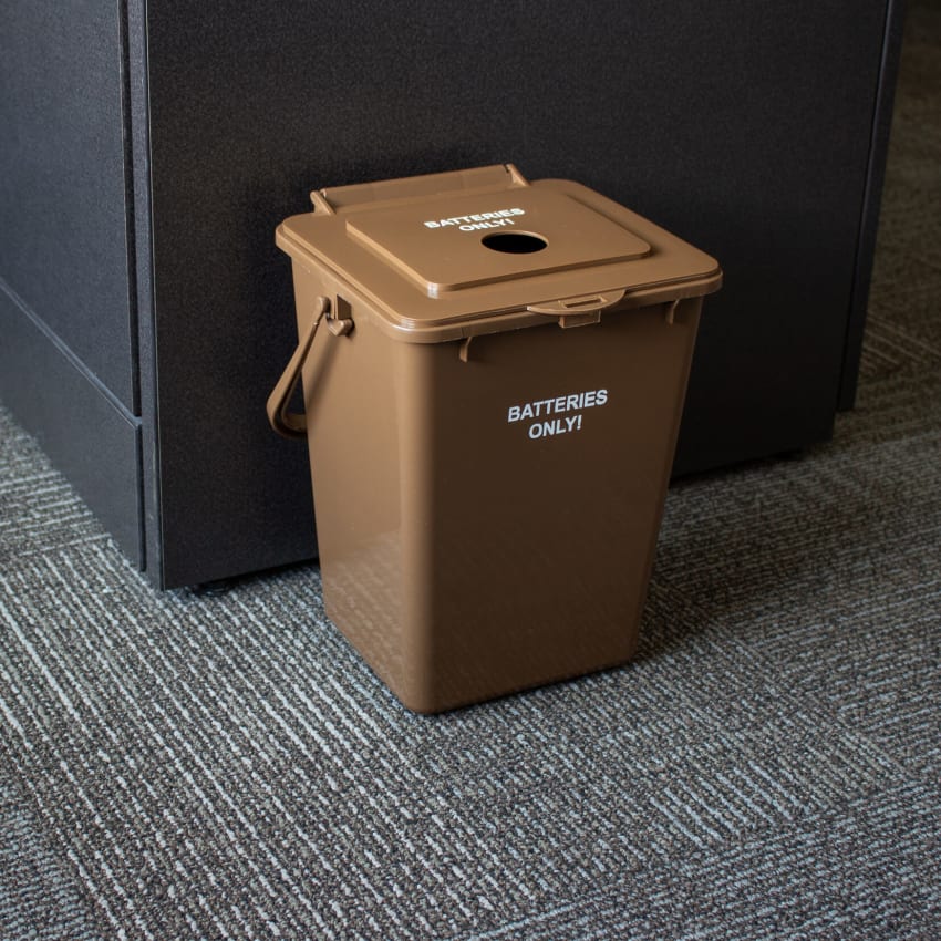 brown injection molded plastic bin for collecting used batteries placed on the floor in a corporate office