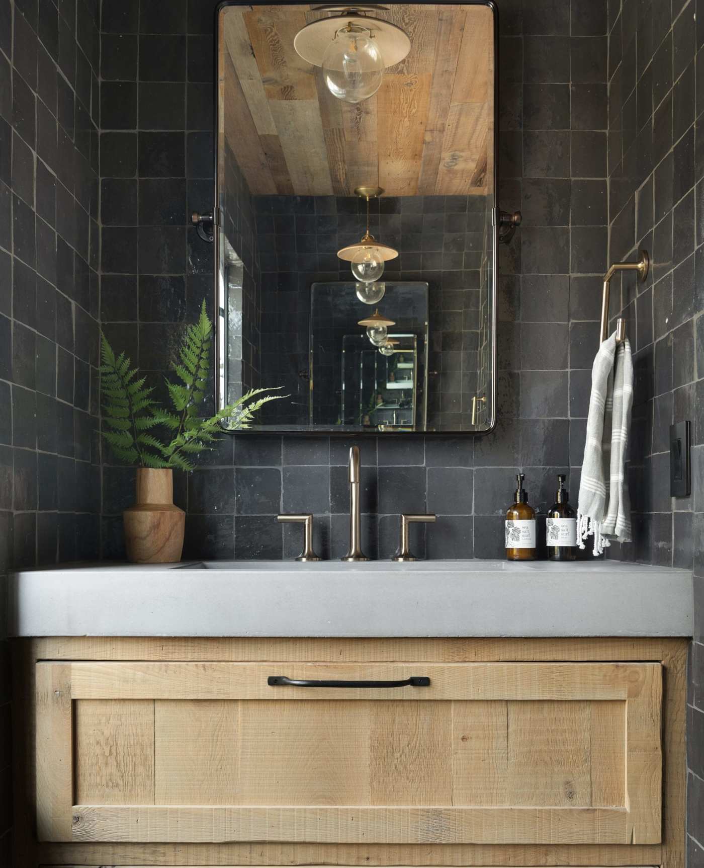 a black tiled bathroom with a wooden vanity and mirror.