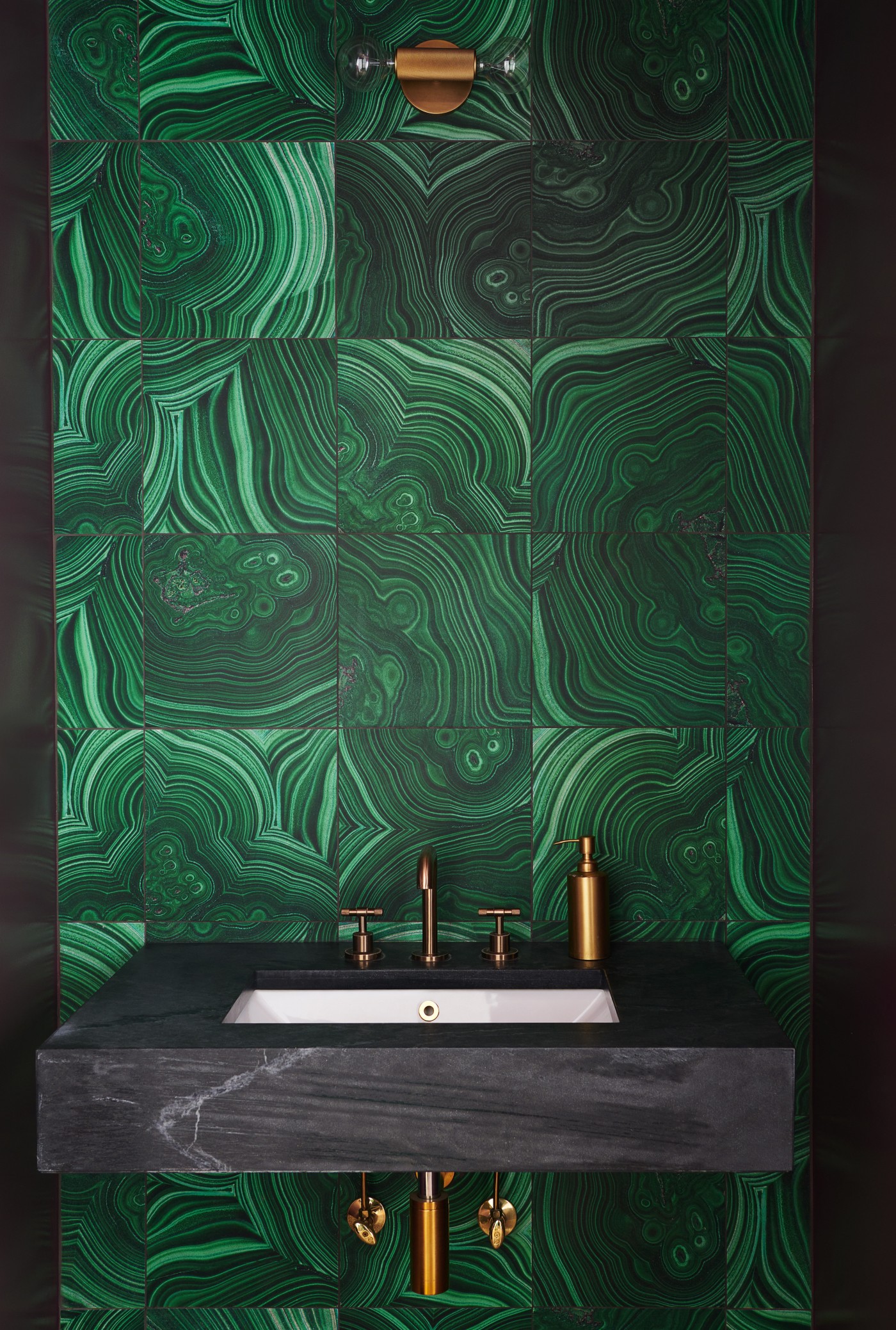 a bathroom with a green patterned tile wall and a black slate sink.