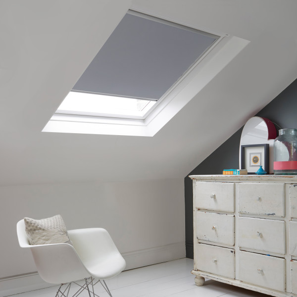 Room with white eaves wall, dark blue-grey wall to right with a shabby chic white drawer unit, a contemporary white chair, white painted floorboards and a skylight blind in pale charcoal grey.