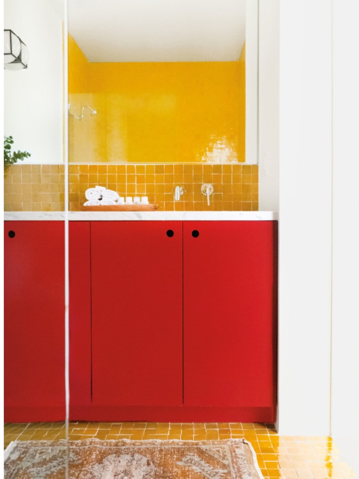 a bathroom with red cabinets and yellow tiled shower walls.