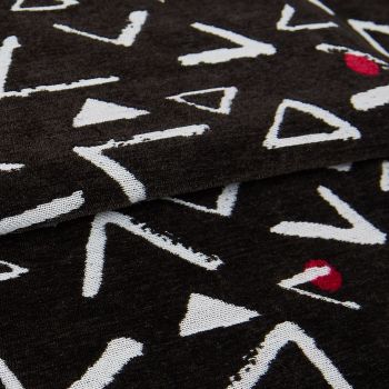 Black knit throw patterned with white, rough-edged triangles and occasional red semicircles; folded in overlapping layers, displaying textured weave and seams in a close-up, softly lit studio view.