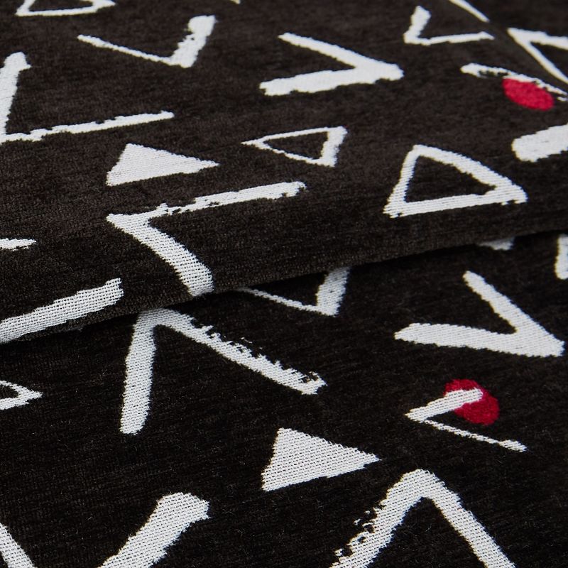 Black knit throw patterned with white, rough-edged triangles and occasional red semicircles; folded in overlapping layers, displaying textured weave and seams in a close-up, softly lit studio view.