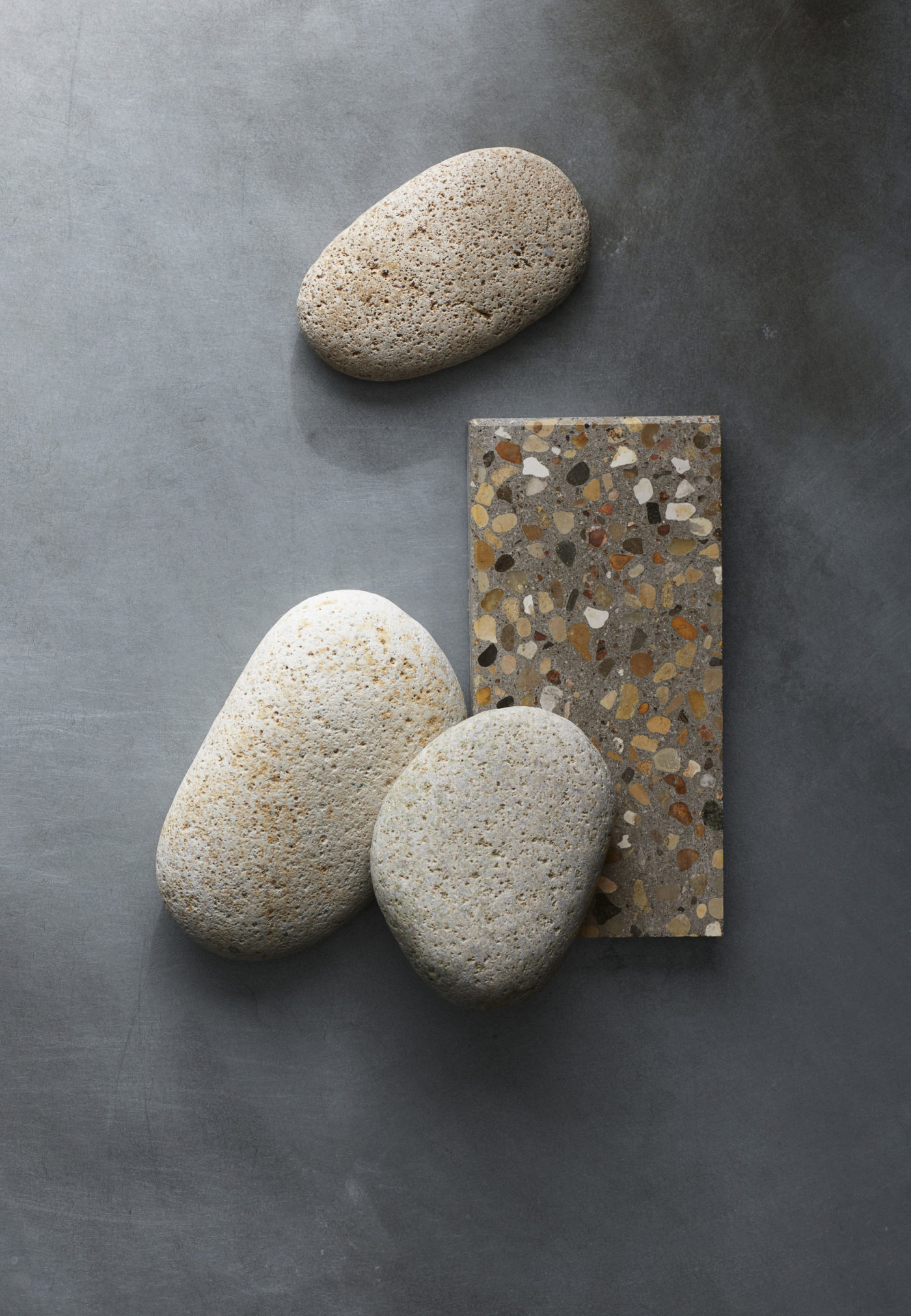 three stones laying near a grey terrazzo tile on a grey surface.