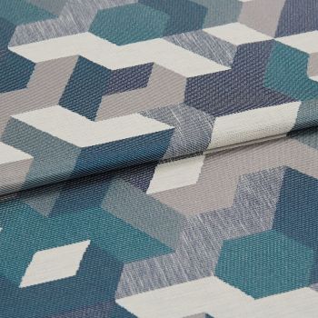Woven upholstery fabric with teal, navy, gray and white isometric geometric pattern â€” folded once, overlapping â€” close-up on a flat surface under soft, neutral lighting.