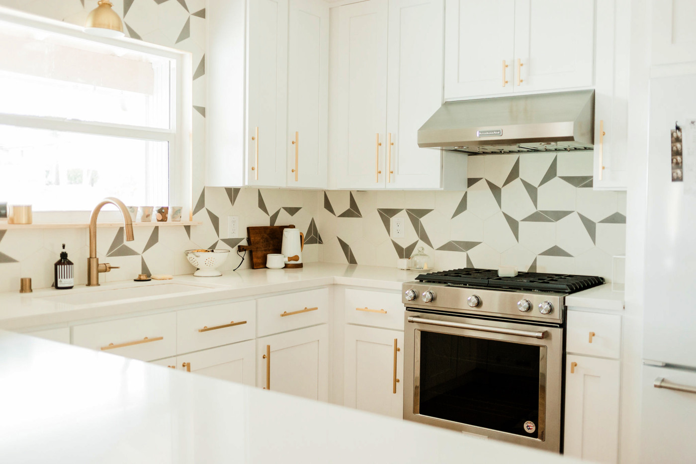 a white kitchen with grey and white geometric tiles on the walls.