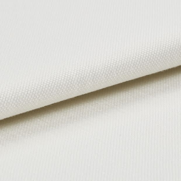 Cream-coloured textured canvas fabric, folded with one layer overlapping another, showing tight plain weave; photographed under soft studio lighting on a neutral background, close-up detail of surface.