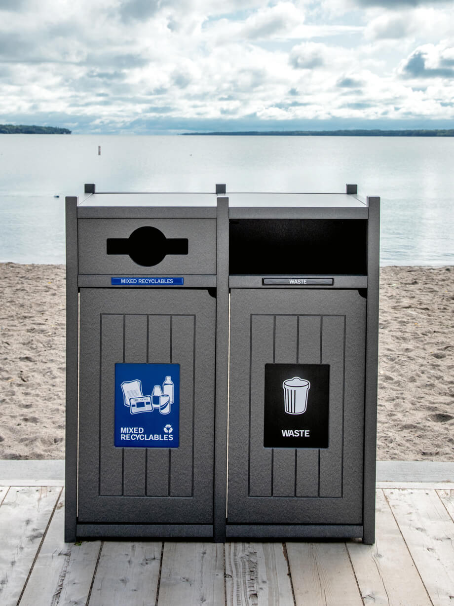 double waste and recycling bin made from recycled plastics with a mixed restrictive opening sitting on the boardwalk at the beach