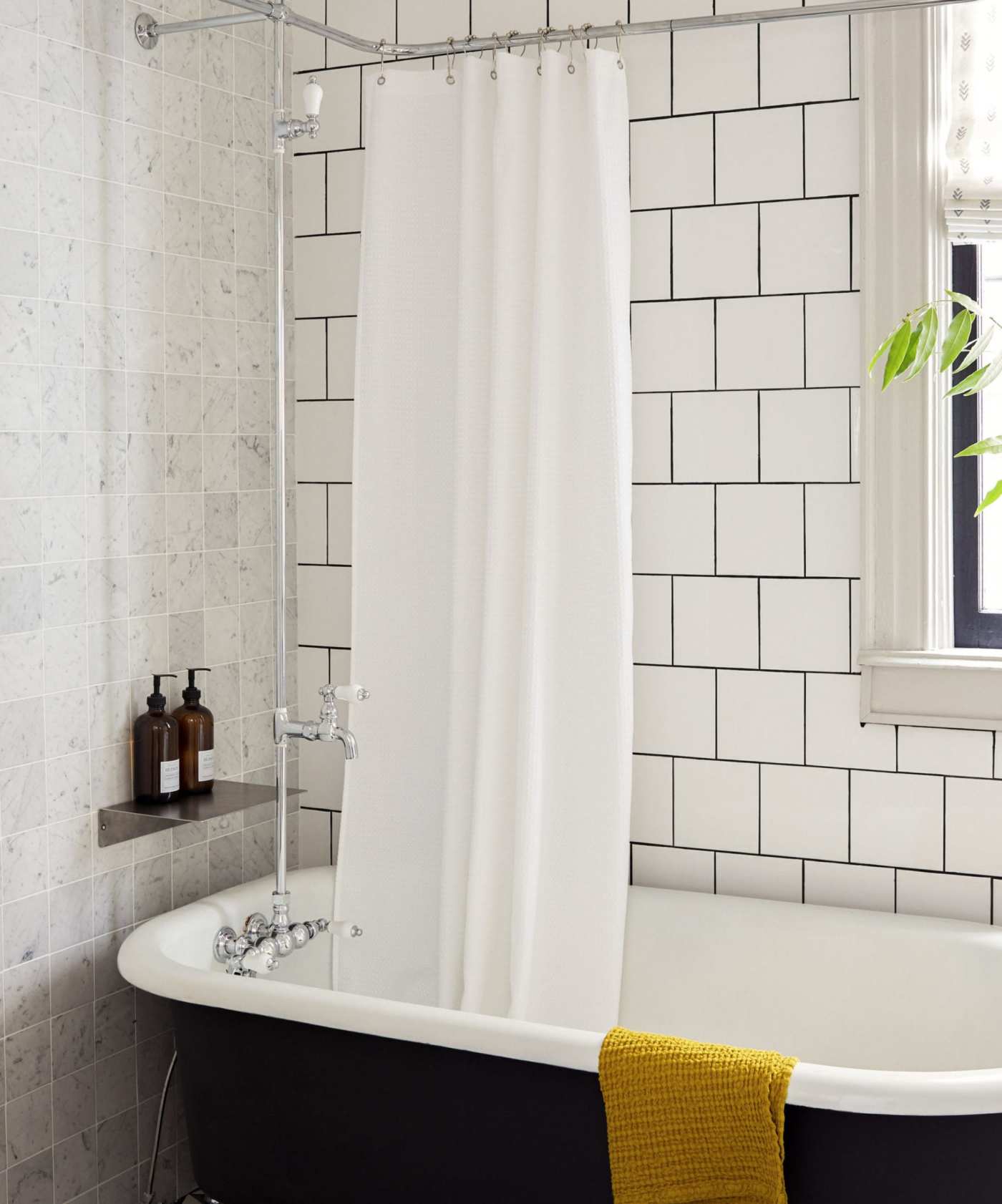 a white tile bathroom with a black tub and white shower curtain.