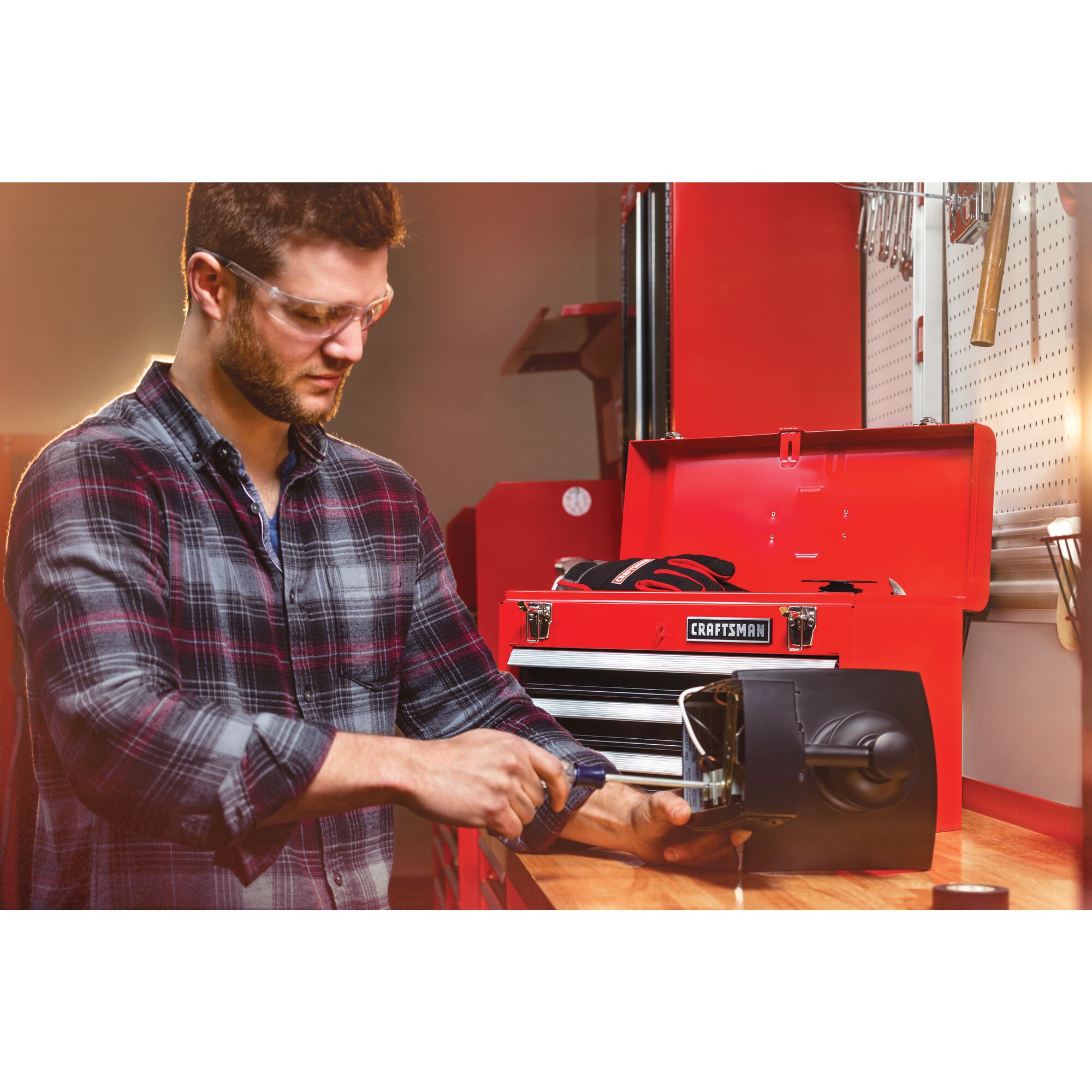 Portable 20 and 5 tenths inch Ball bearing 3 Drawer Red Steel Lockable Tool Box containing tools in use by person working on inner mechanism of a device.
