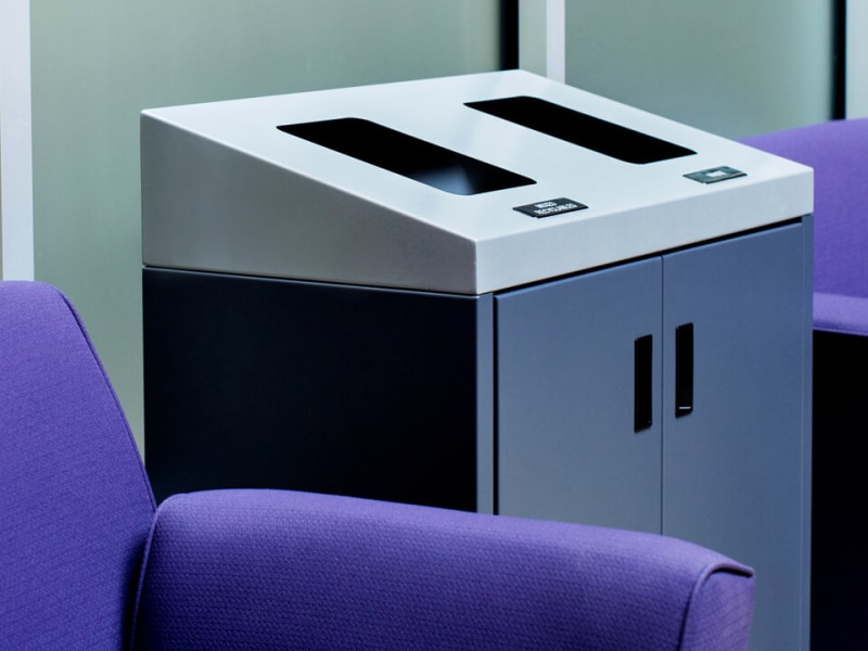double trash and recycling container with a sloped lid made from durable powder coated steel in a busy college campus