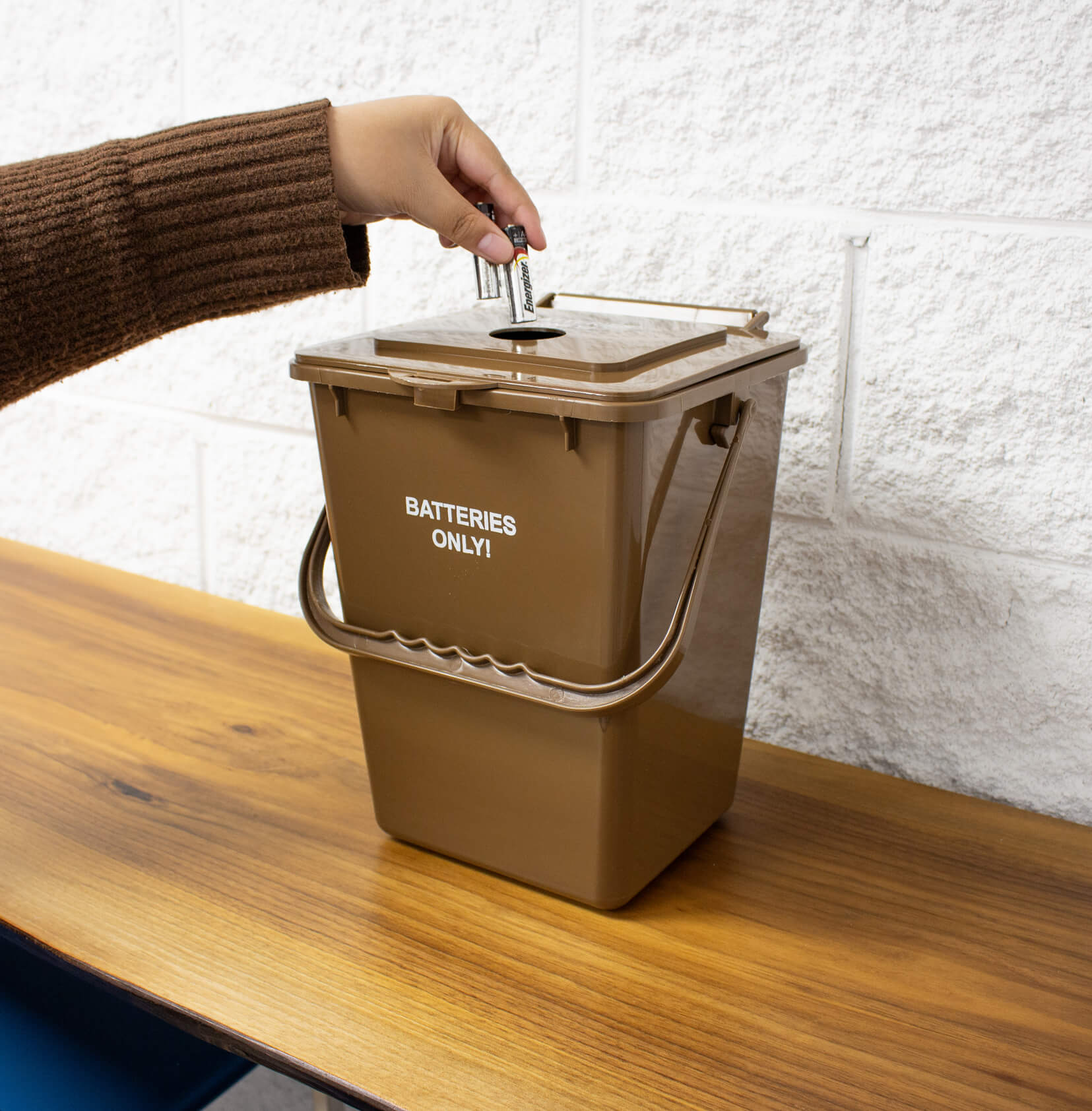 brown plastic container for collecting used battering for recycling placed on a wood shelf with a person depositing batteries
