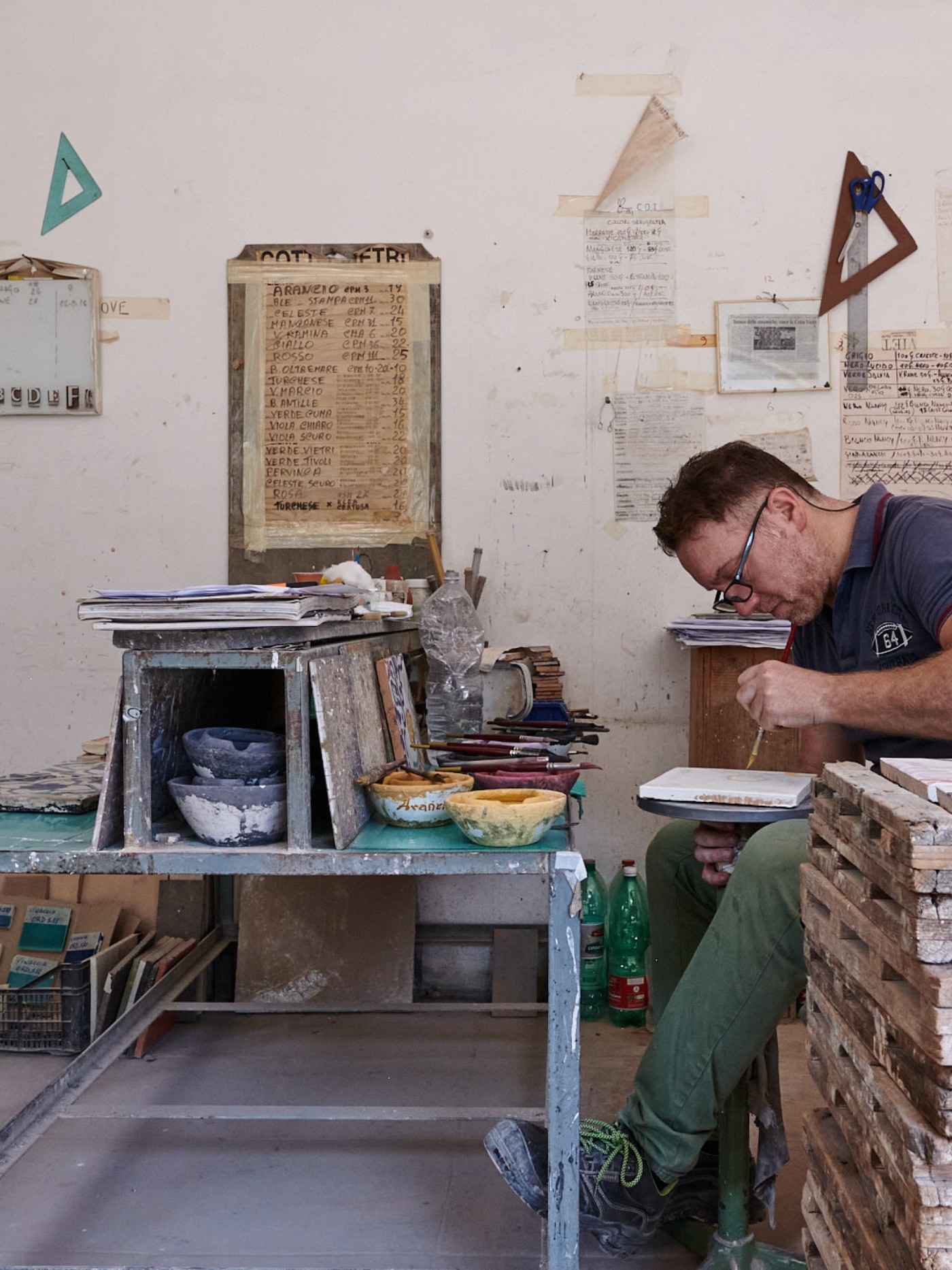 a man hand painting a tile in a workshop.