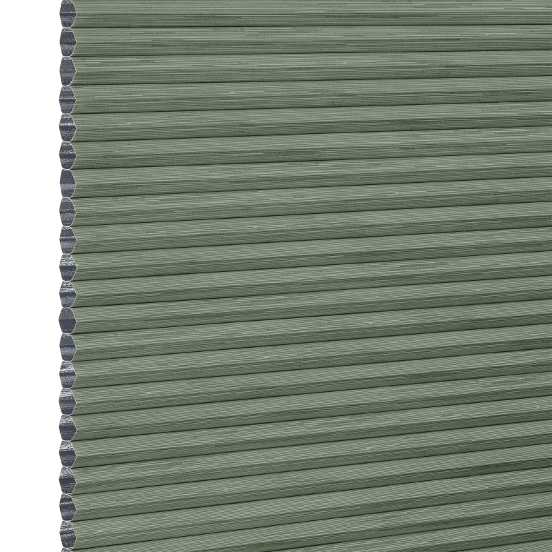 Cellular honeycomb blind â€” sage-green pleated fabric fully lowered with exposed hexagonal cells along the left edge; blocking and softly filtering light in a neutral interior.