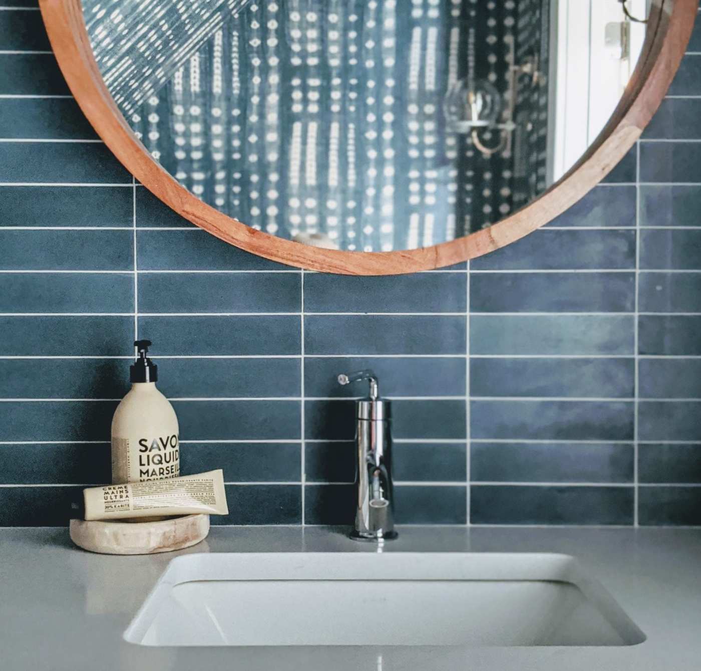 a bathroom sink with a blue tiled backsplash and a round mirror.