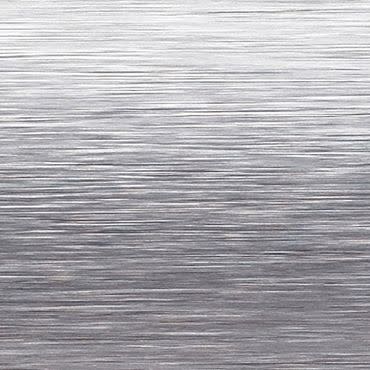 Brushed stainless-steel surface with fine horizontal grain; reflecting diffuse light and subtle highlights, close-up view suggesting a sheet-metal or appliance panel in a neutral, evenly lit studio context.